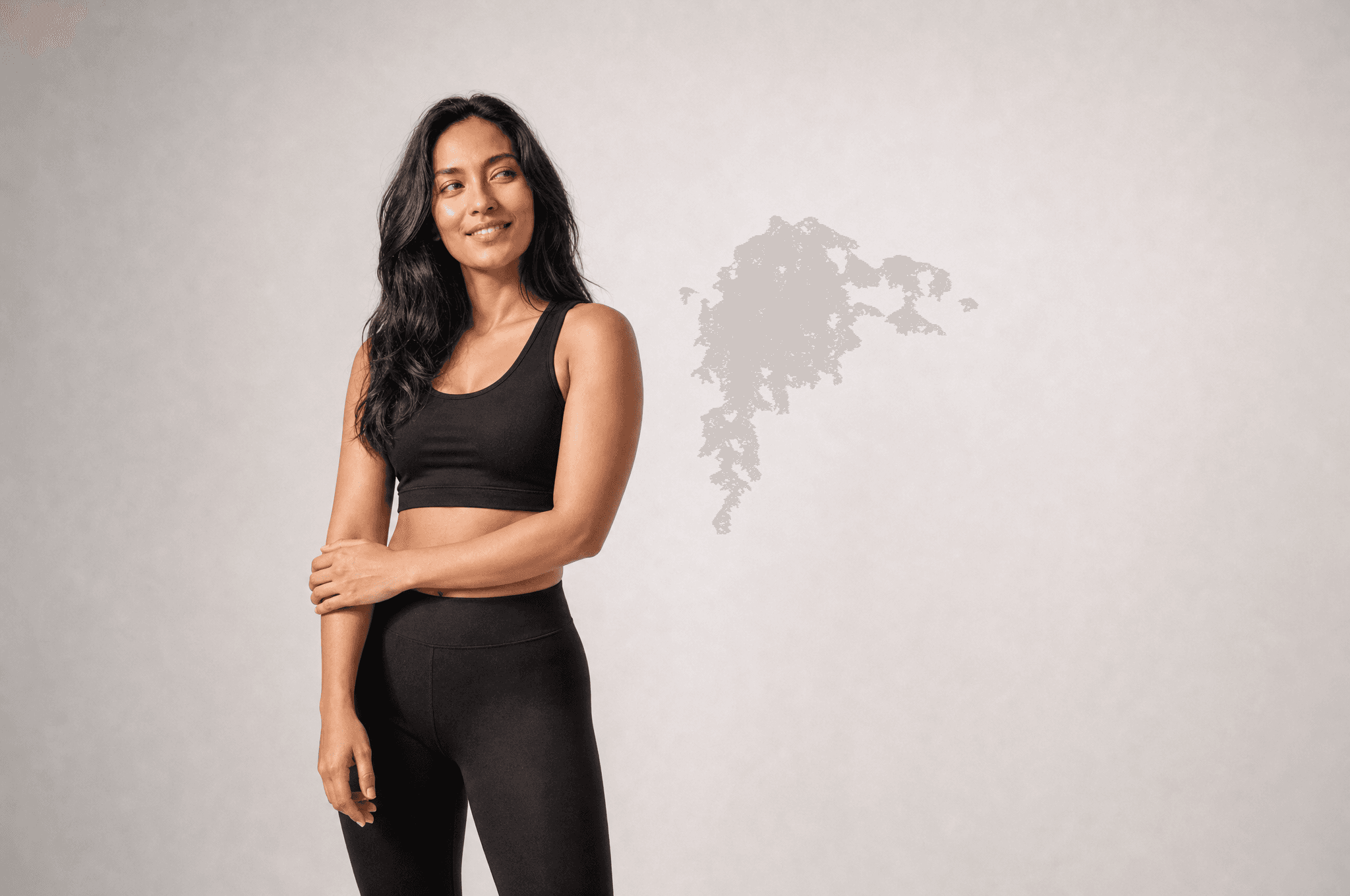 A woman in black athleisure standing three-quarter to camera in a white studio, one hand on her forearm