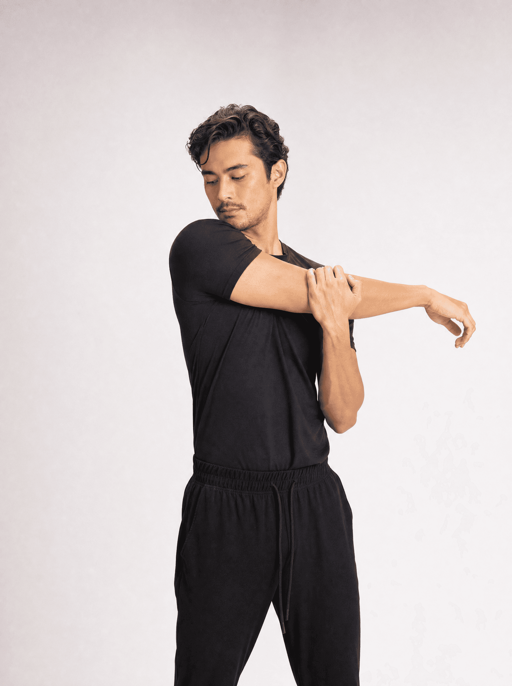 Man in a black tee in a controlled stretch, warm grey studio
