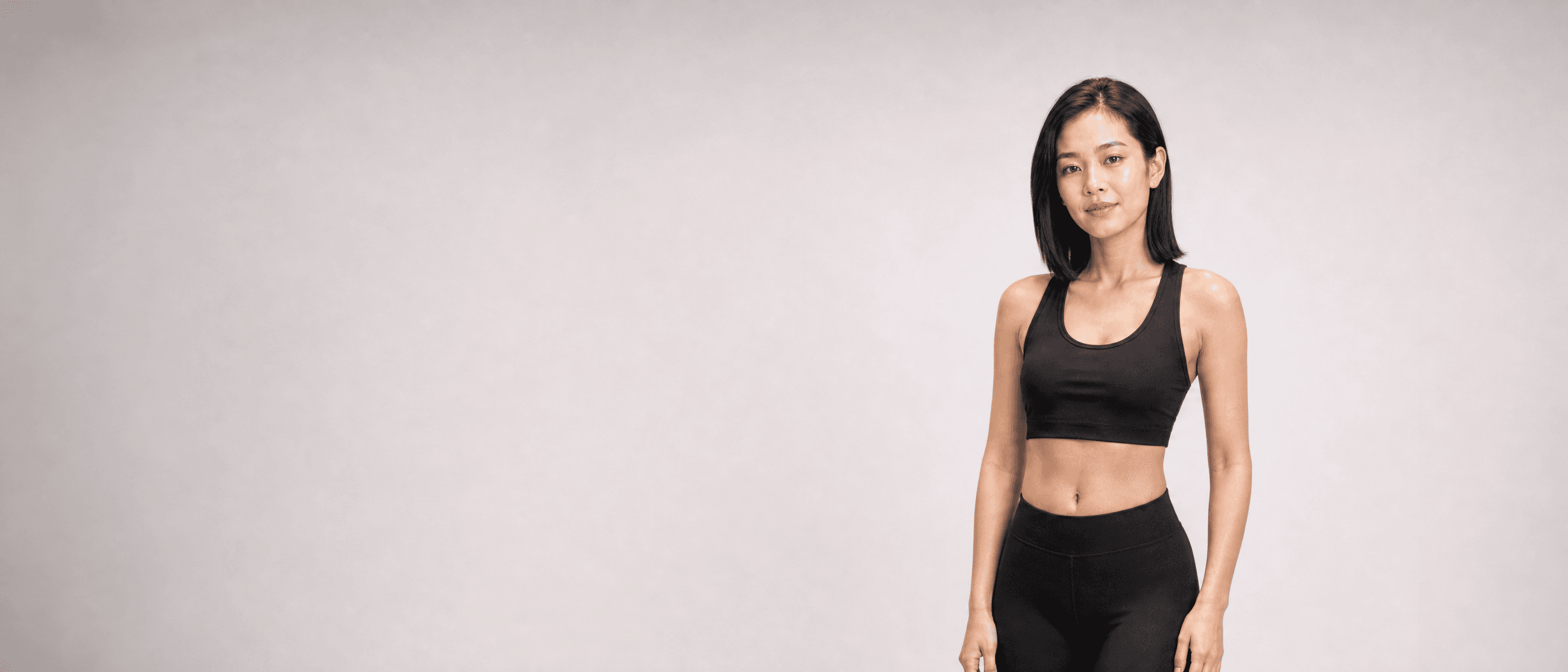 A woman in black athleisure standing square to camera in a white studio, arms loose at her sides