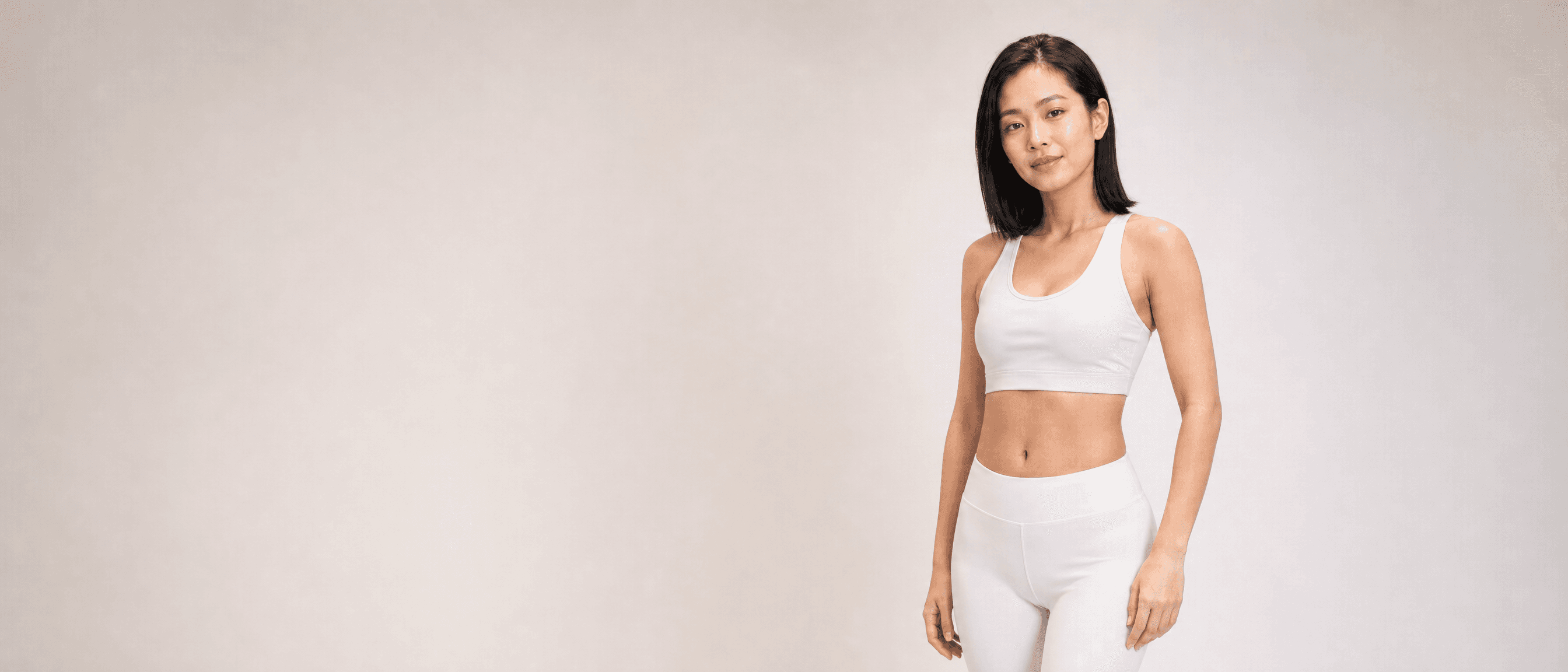 A woman in white athleisure standing three-quarter to camera in a white studio, one hand at her side