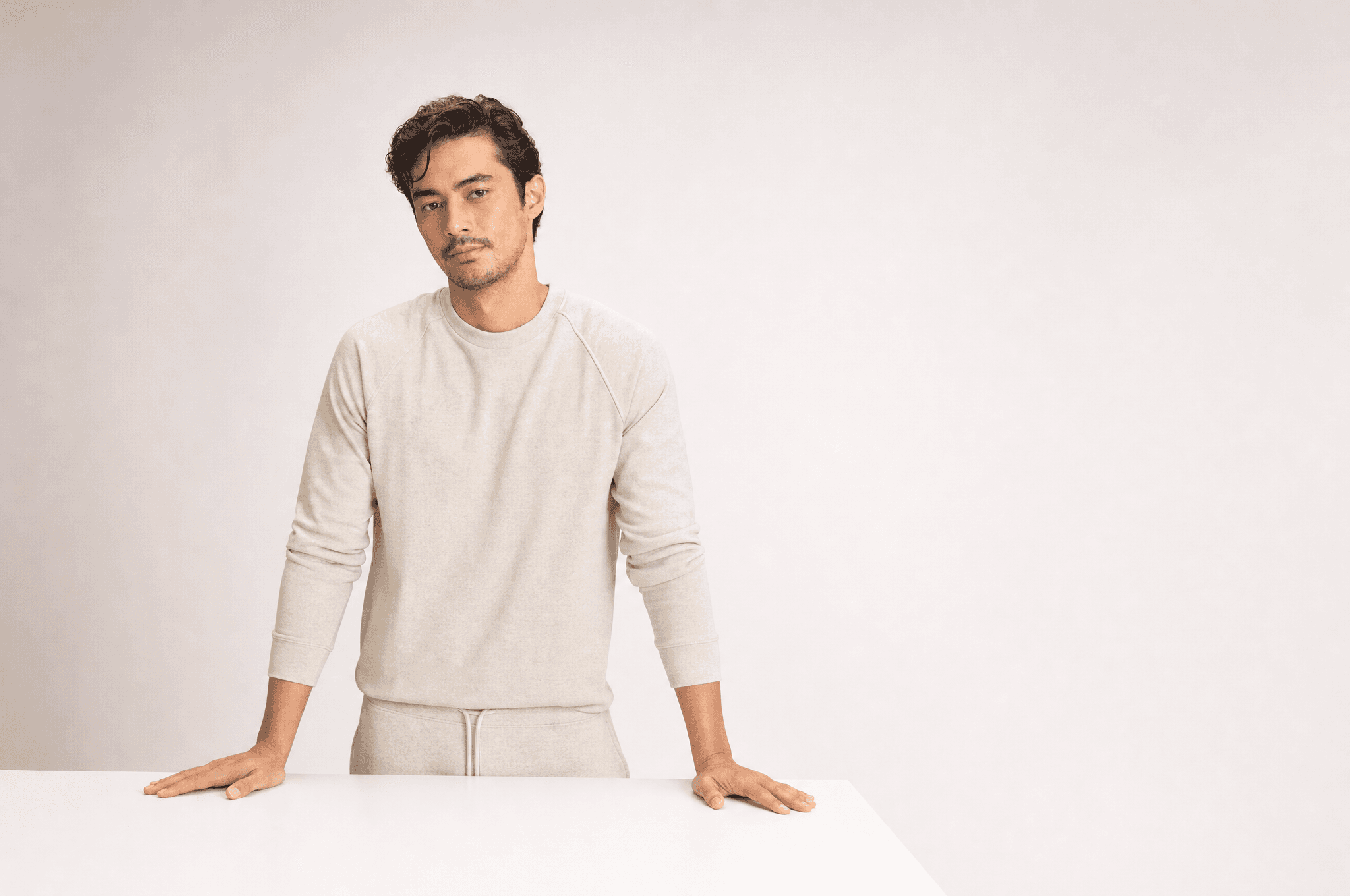 A man in oat loungewear standing at an empty white counter with both hands resting on it