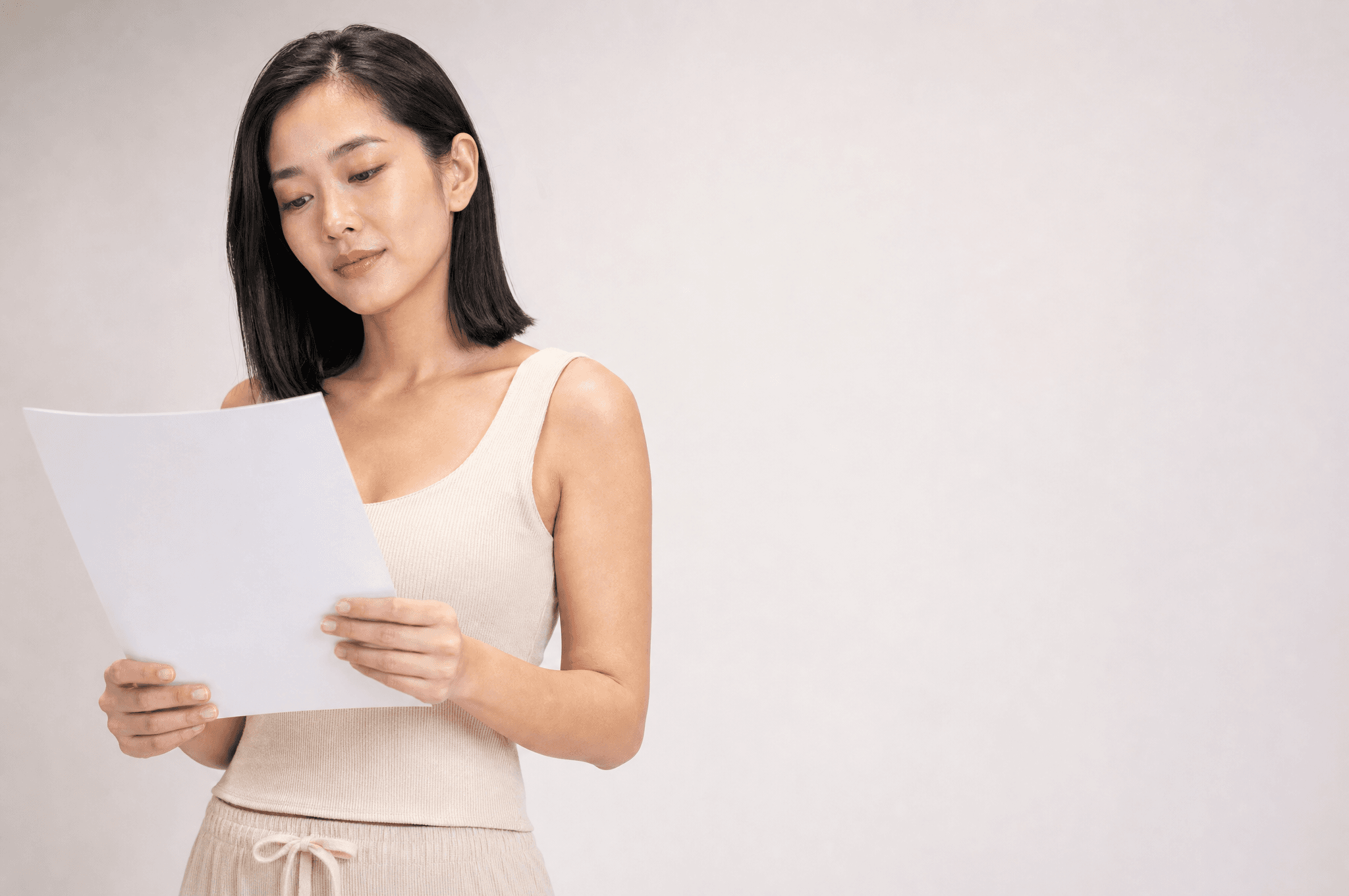 Close portrait of a woman in an oat top reading a single white page in soft studio light