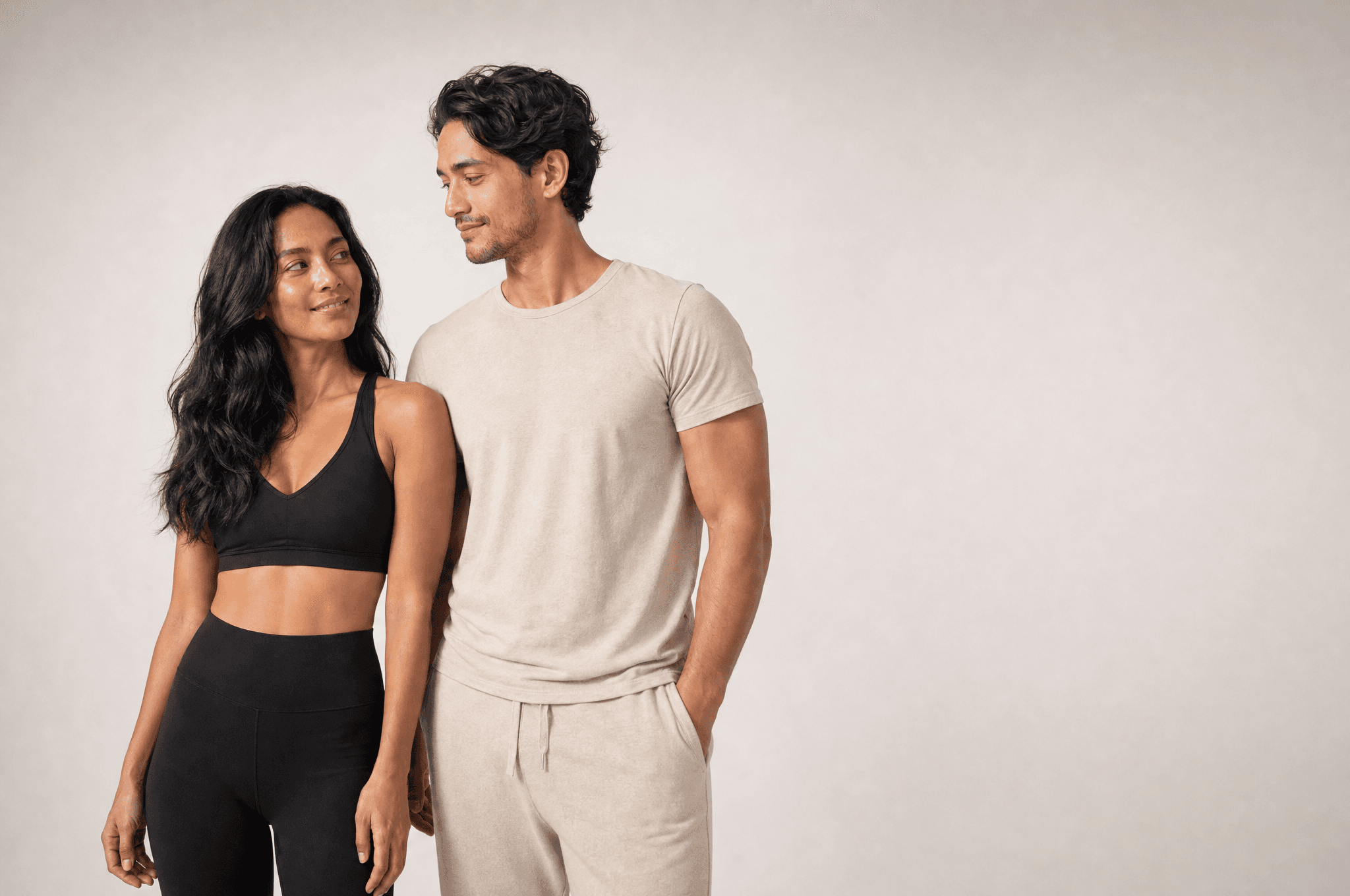 A woman and a man standing side by side in a white studio, turned toward each other, deciding
