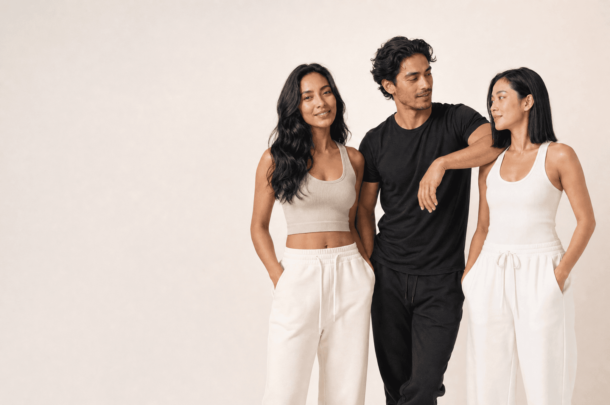 Three people standing loosely together on the right of a white studio, one looking at camera