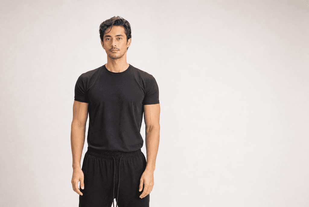 A man in a black tee standing square to camera in a white studio, arms loose at his sides