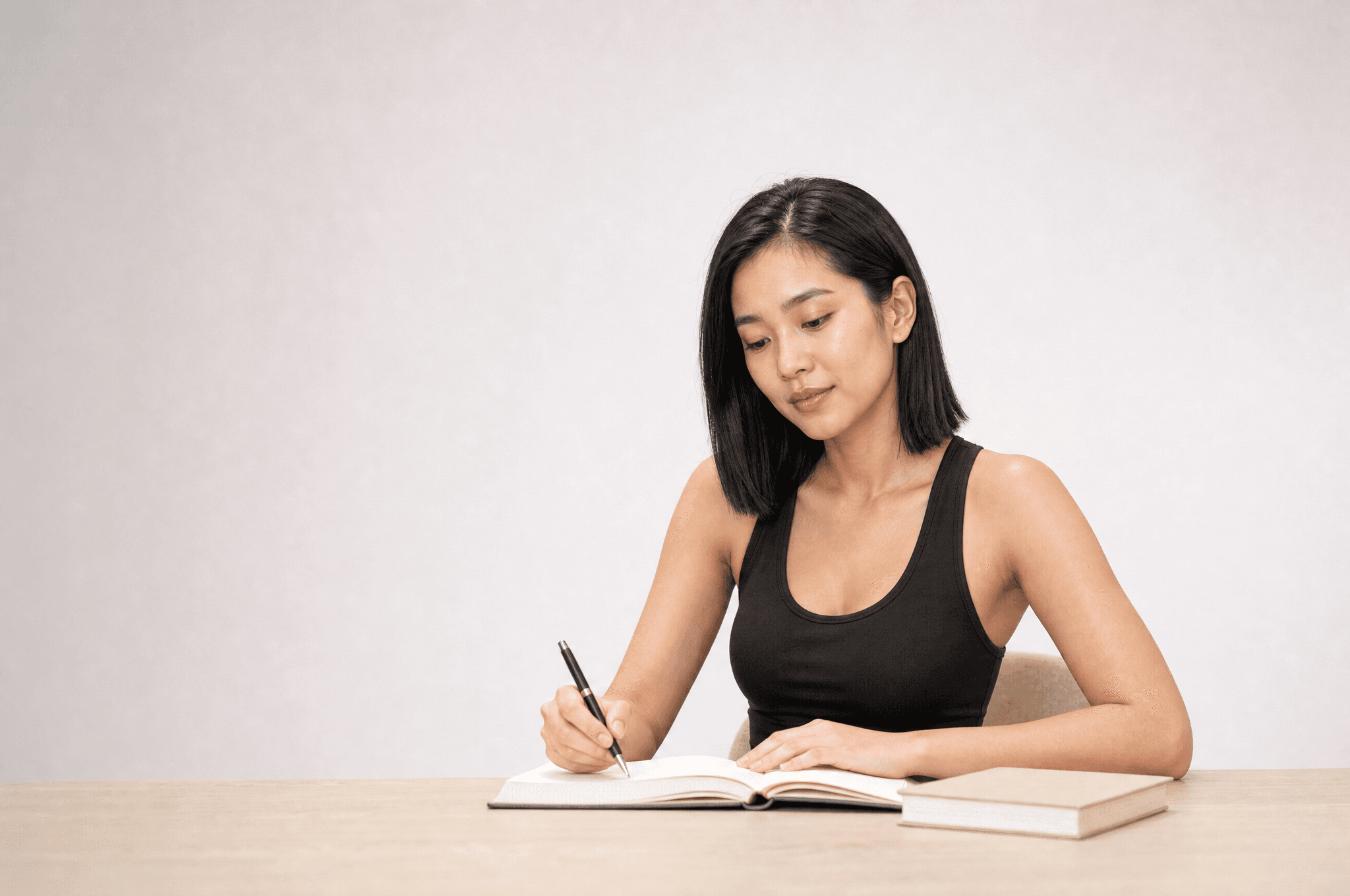A woman in black loungewear writing in an open notebook at a pale wood desk