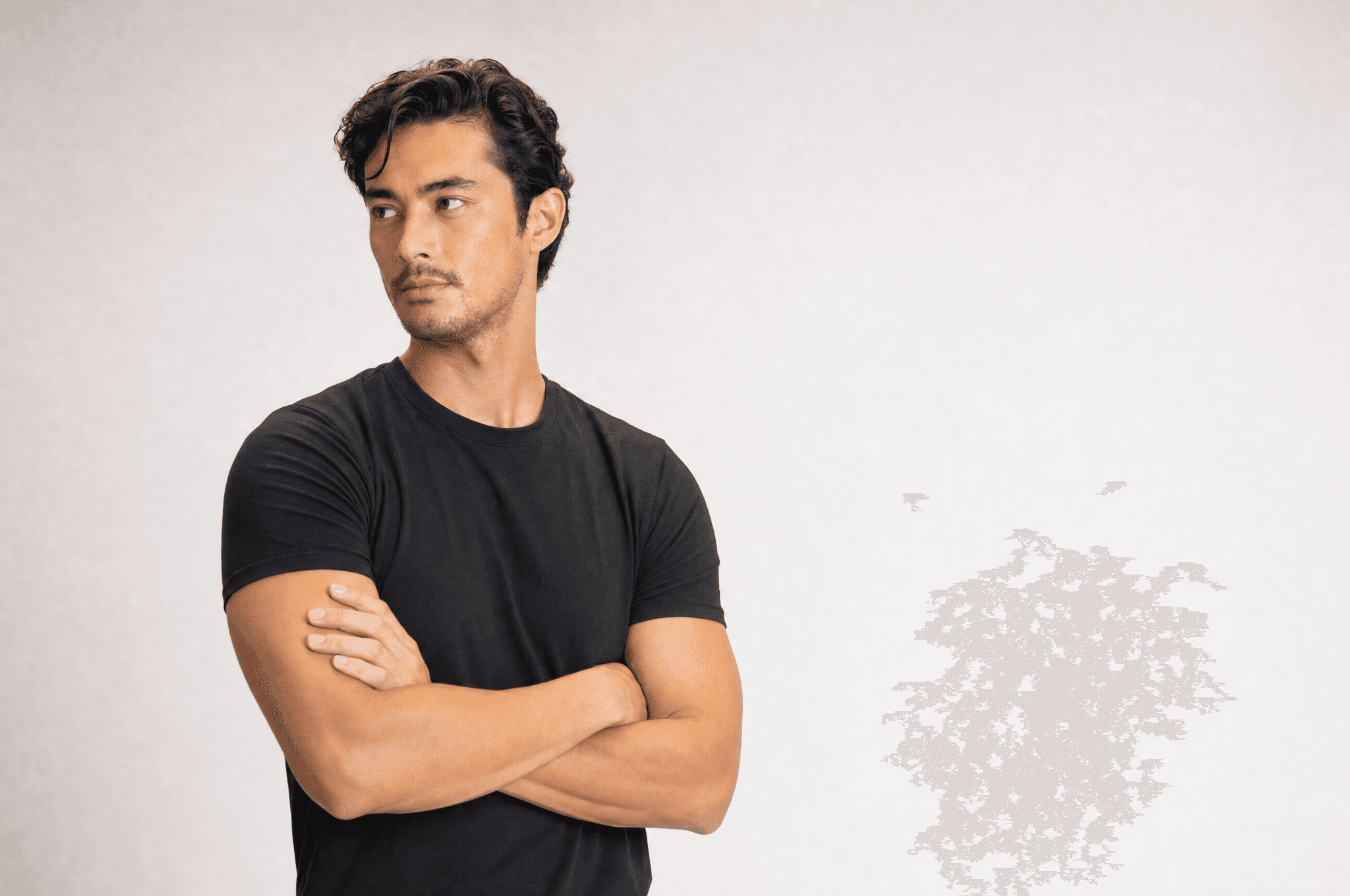 A man in a black tee with his arms crossed loosely, looking off past the camera, thinking