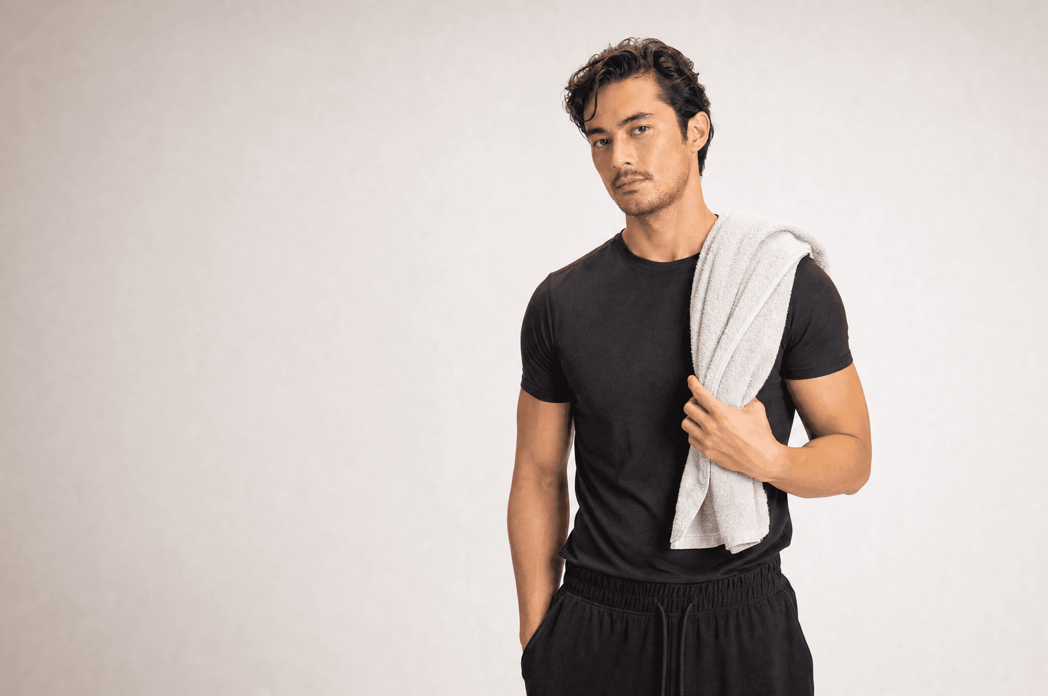 A man in black athleisure with a folded pale towel over one shoulder, looking at camera