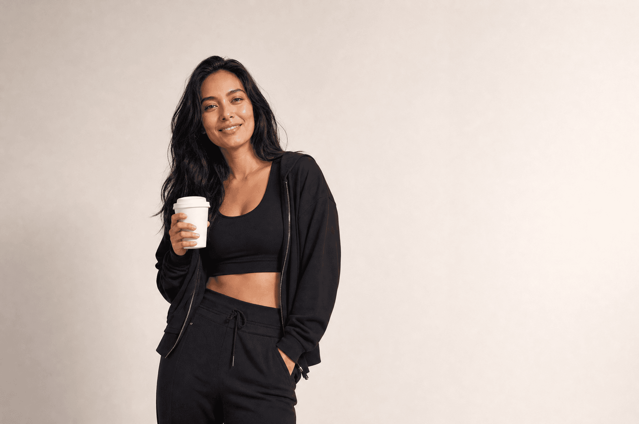 A woman in black athleisure holding a plain takeaway coffee cup, looking at camera