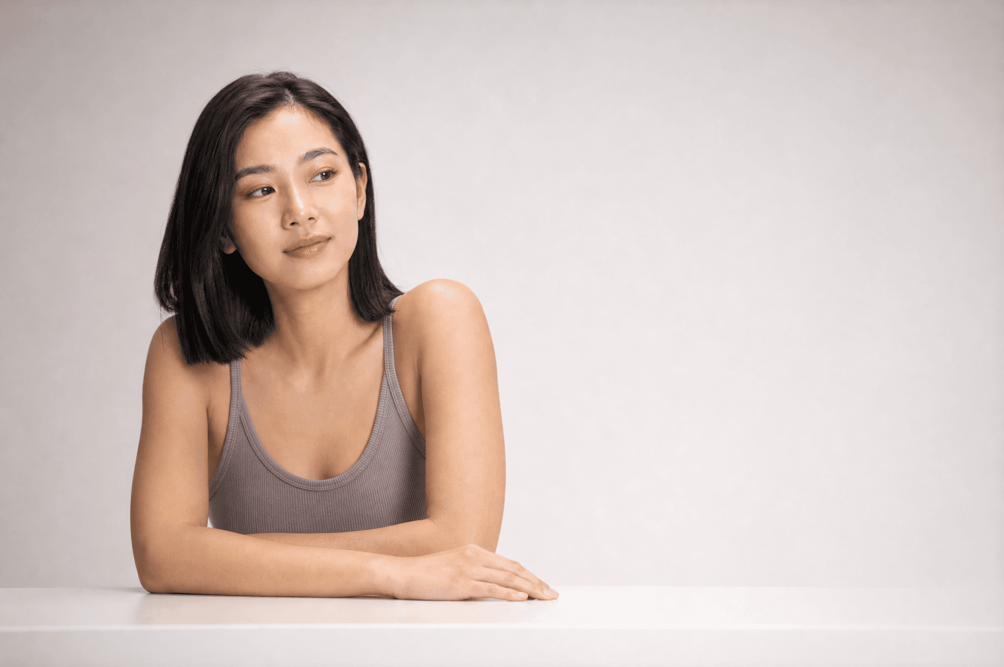 A woman in warm grey loungewear resting both forearms on a white counter, looking off to one side